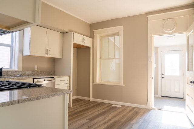 kitchen featuring stainless steel dishwasher, light stone counters, white cabinetry, and light hardwood / wood-style flooring