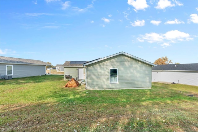 rear view of property featuring a yard, central AC unit, and solar panels