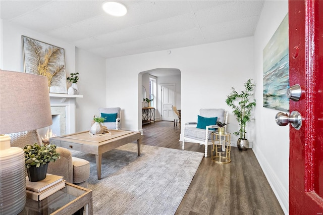 living area featuring arched walkways, a warm lit fireplace, baseboards, and wood finished floors