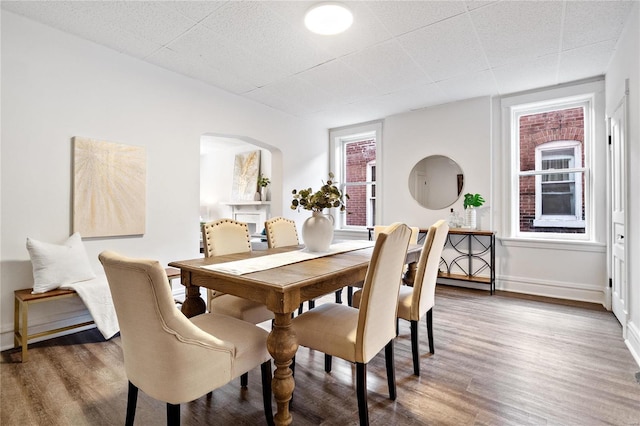 dining area with baseboards, arched walkways, and wood finished floors