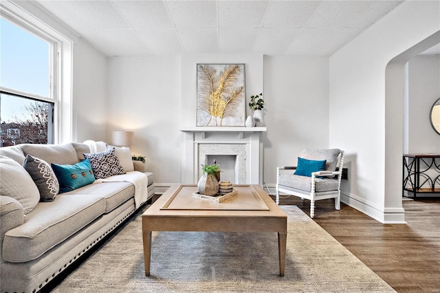 living area with arched walkways, a fireplace, wood finished floors, and baseboards