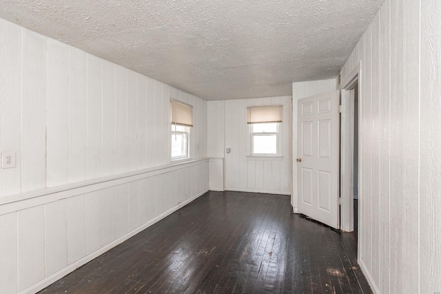 empty room featuring dark hardwood / wood-style floors, a textured ceiling, and wooden walls