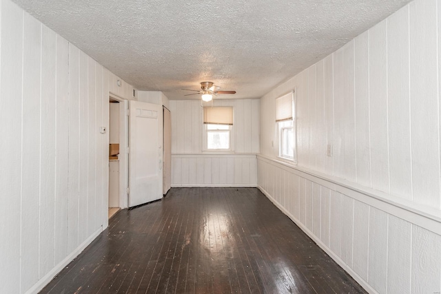 spare room featuring ceiling fan, dark hardwood / wood-style flooring, wood walls, and a textured ceiling