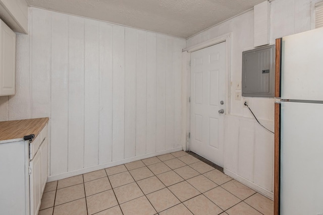 kitchen with electric panel, white refrigerator, wooden walls, light tile patterned floors, and white cabinetry