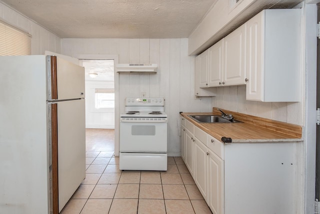 kitchen featuring white appliances, white cabinets, sink, wooden walls, and light tile patterned flooring