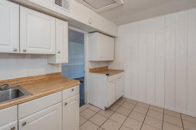 kitchen with white cabinets, light tile patterned floors, sink, and wooden walls