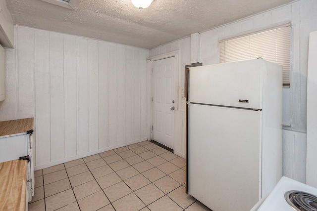 kitchen with light tile patterned floors, white refrigerator, a textured ceiling, and wooden walls