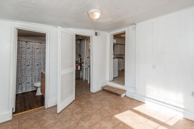 unfurnished bedroom featuring a textured ceiling, connected bathroom, light parquet floors, and washer / dryer