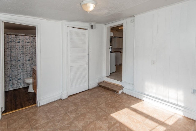 unfurnished bedroom featuring connected bathroom, a closet, a textured ceiling, and washer / dryer