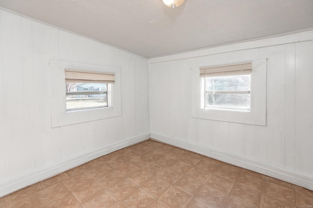 spare room with wood walls, a textured ceiling, a wealth of natural light, and light parquet floors