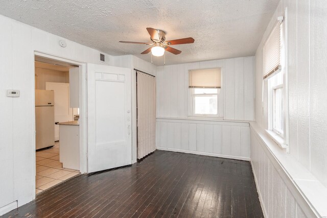 unfurnished bedroom with a textured ceiling, a ceiling fan, a closet, freestanding refrigerator, and hardwood / wood-style floors