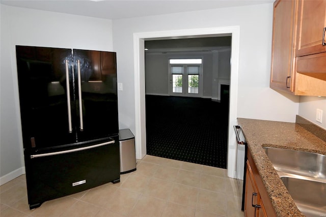 kitchen featuring black fridge, sink, light tile patterned floors, and dark stone counters