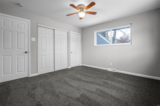 unfurnished bedroom with dark colored carpet, ceiling fan, and multiple closets