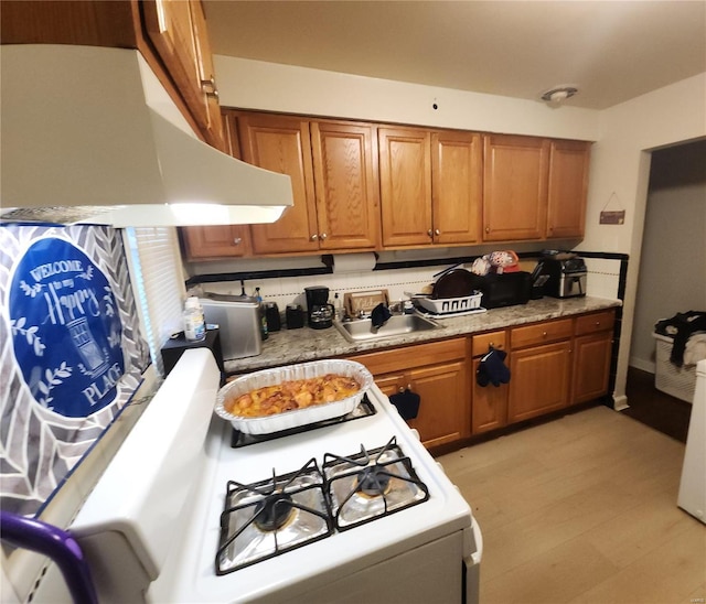 kitchen featuring brown cabinets, a sink, gas range gas stove, and ventilation hood