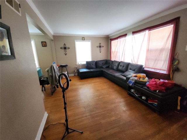 living area with baseboards, wood finished floors, visible vents, and crown molding