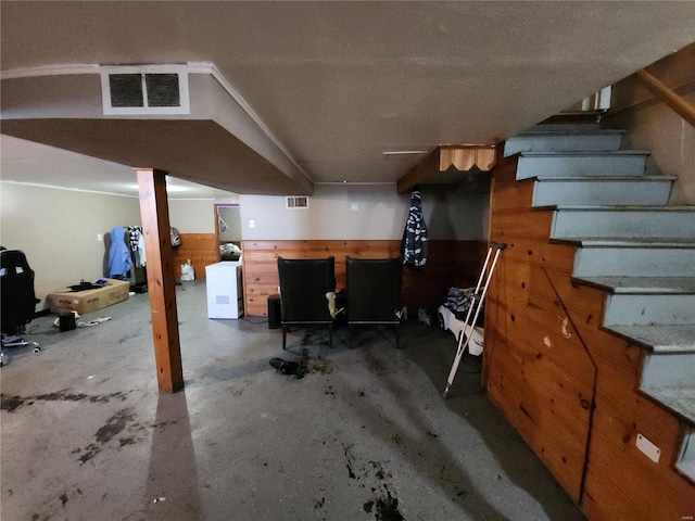 finished basement with a wainscoted wall, visible vents, wood walls, and stairs