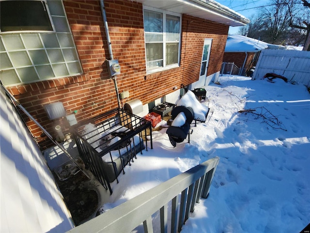 view of snow covered exterior with fence and brick siding