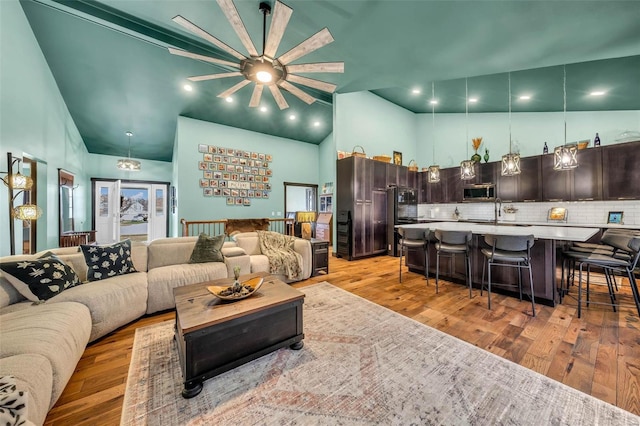 living room featuring ceiling fan, a towering ceiling, sink, and light hardwood / wood-style flooring