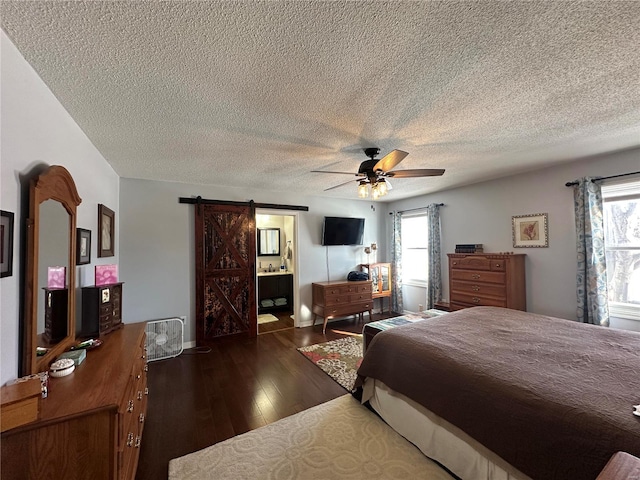 bedroom featuring connected bathroom, a barn door, ceiling fan, dark wood-type flooring, and a textured ceiling