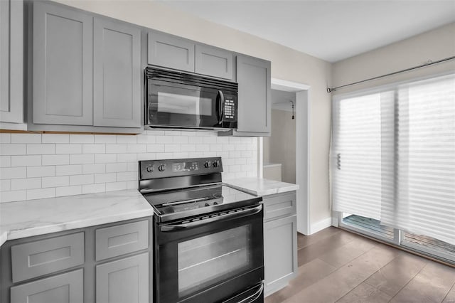 kitchen with light stone countertops, tasteful backsplash, black appliances, gray cabinets, and light hardwood / wood-style floors