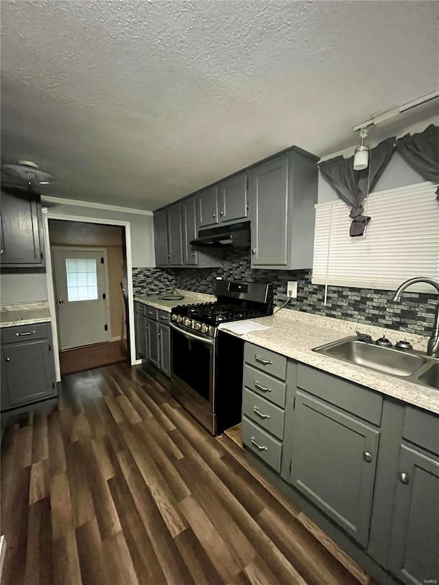 kitchen with decorative backsplash, dark hardwood / wood-style flooring, stainless steel gas range oven, a textured ceiling, and sink