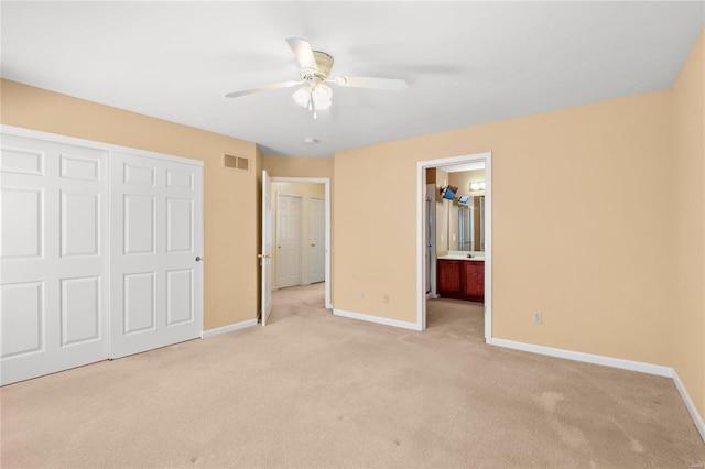 unfurnished bedroom featuring ceiling fan, light colored carpet, ensuite bathroom, and a closet