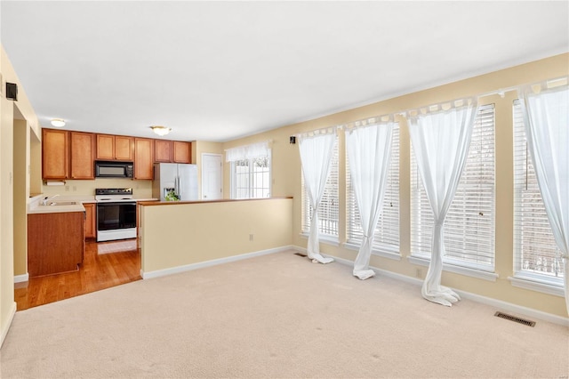 kitchen featuring white range with electric stovetop, stainless steel fridge, a healthy amount of sunlight, and light carpet