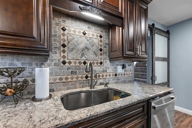 kitchen featuring light stone countertops, sink, tasteful backsplash, a barn door, and dark hardwood / wood-style floors