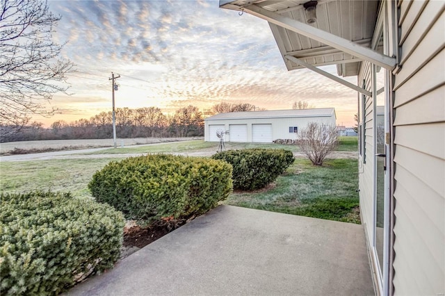 yard at dusk with a garage, an outbuilding, and a patio