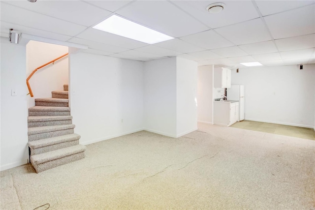 basement featuring a drop ceiling, white refrigerator, and light carpet