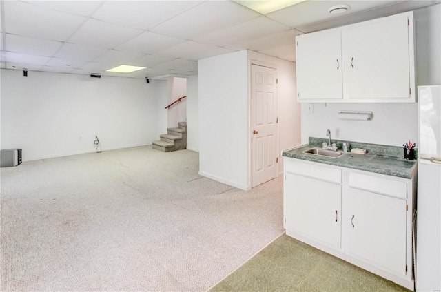 kitchen with a paneled ceiling, white cabinetry, sink, and light colored carpet