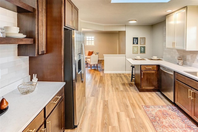 kitchen with backsplash, a skylight, light wood-type flooring, kitchen peninsula, and stainless steel appliances