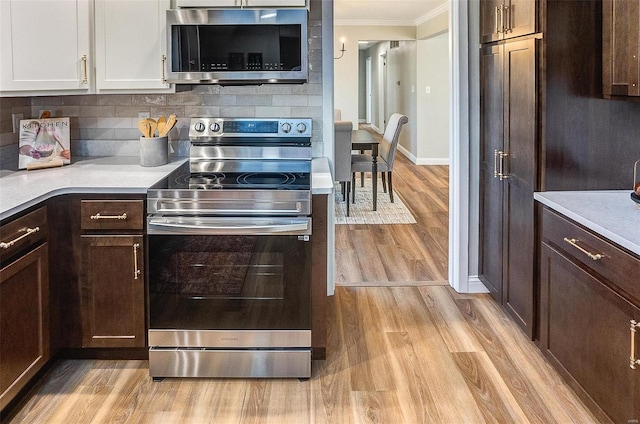 kitchen featuring white cabinetry, stainless steel appliances, backsplash, light hardwood / wood-style floors, and ornamental molding