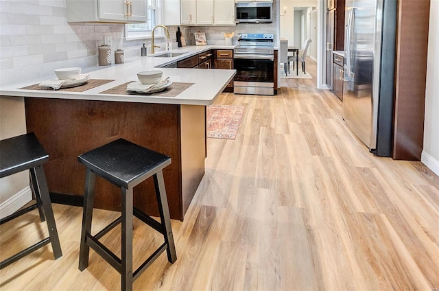 kitchen with kitchen peninsula, a kitchen breakfast bar, stainless steel appliances, sink, and white cabinets