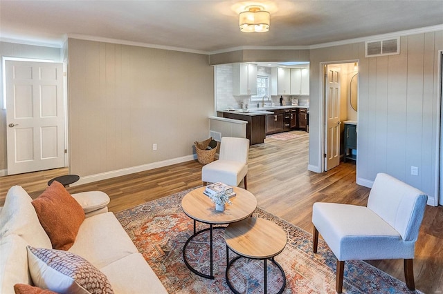 living room with wood walls, sink, ornamental molding, and light wood-type flooring