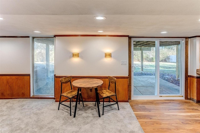 dining space with wooden walls, ornamental molding, indoor bar, and light wood-type flooring