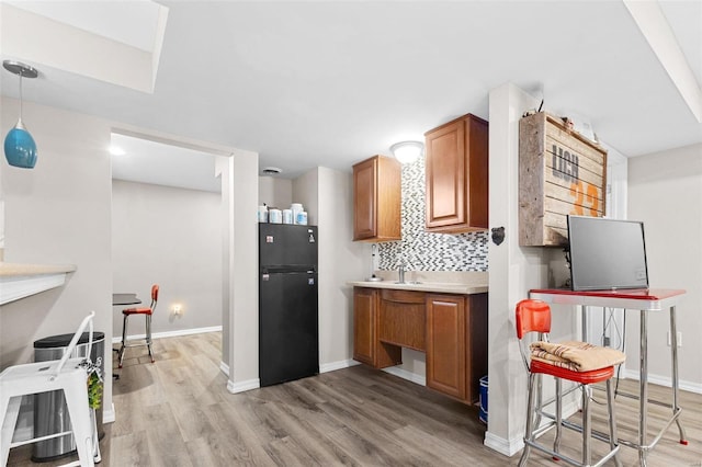 kitchen with black refrigerator, pendant lighting, tasteful backsplash, and light hardwood / wood-style floors