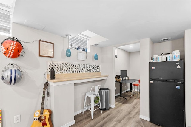 kitchen featuring decorative backsplash, light hardwood / wood-style flooring, black fridge, and hanging light fixtures