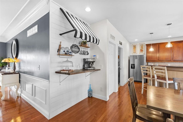 interior space featuring dark wood-type flooring, kitchen peninsula, stainless steel fridge, pendant lighting, and a kitchen bar