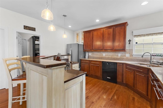 kitchen featuring sink, hanging light fixtures, black dishwasher, wood-type flooring, and a breakfast bar