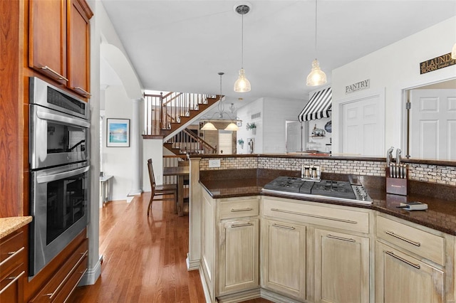 kitchen featuring decorative backsplash, appliances with stainless steel finishes, ornate columns, decorative light fixtures, and hardwood / wood-style floors