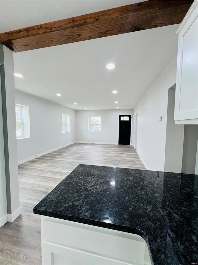 kitchen with dark stone counters, beamed ceiling, white cabinets, and light hardwood / wood-style floors