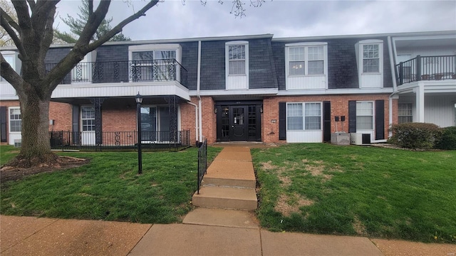 view of property with cooling unit, mansard roof, a front lawn, brick siding, and a shingled roof