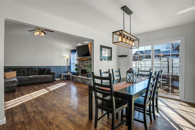 dining space featuring ceiling fan with notable chandelier, a fireplace, and hardwood / wood-style flooring