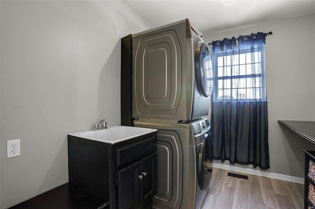 washroom featuring hardwood / wood-style flooring, stacked washer / dryer, and sink