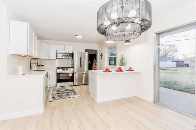 kitchen featuring pendant lighting, white cabinets, sink, appliances with stainless steel finishes, and light hardwood / wood-style floors