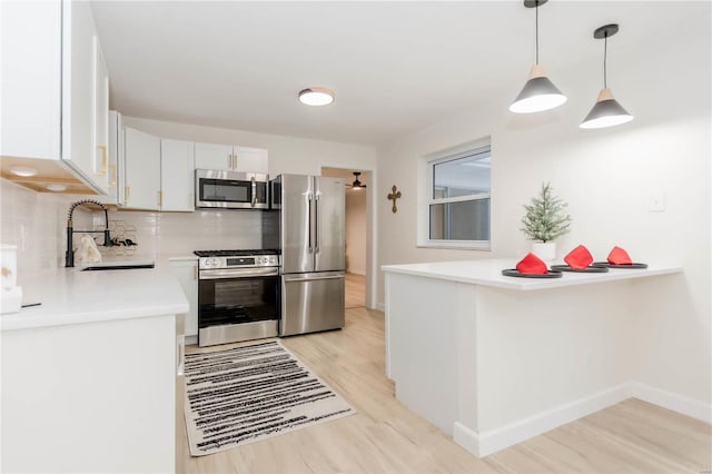 kitchen with light wood-type flooring, stainless steel appliances, sink, pendant lighting, and white cabinetry