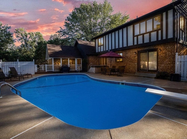 pool at dusk with a patio and a diving board