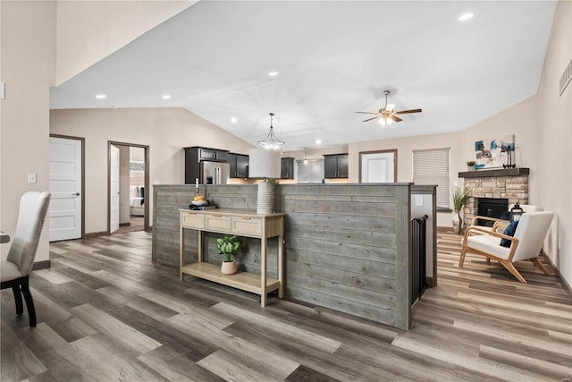 kitchen featuring dark wood-type flooring, a stone fireplace, vaulted ceiling, ceiling fan, and stainless steel fridge