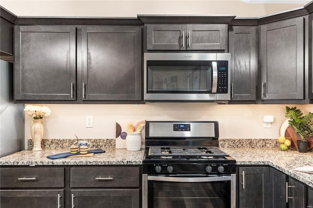 kitchen with dark brown cabinets, light stone counters, and stainless steel appliances